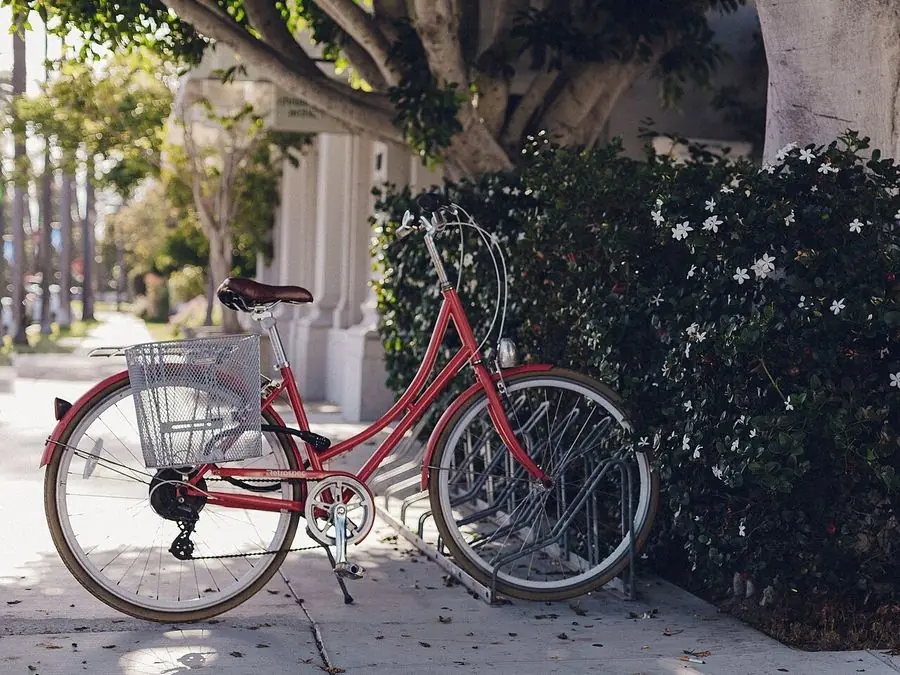 Una bicicleta roja con canasta estacionada en una acera soleada