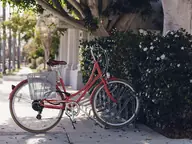 Una bicicleta roja con canasta estacionada en una acera soleada
