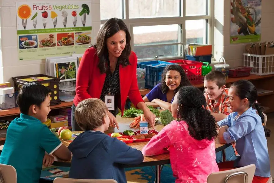Una maestra con alumnos pequeños alrededor de una mesa del salón